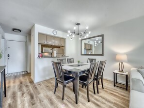 Ein Essbereich mit Holztisch und -stühlen, eine Küche mit Schränken und Geräten, eine Uhr und ein Spiegel an der Wand.