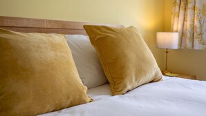 A hotel room with a wooden headboard, two mustard-colored pillows, a white bedspread, and a nightstand with a lamp and a plate. - Cheerful and modern one bedroom home with parking - Pass the Keys (Shrewsbury)