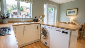 A compact kitchen with a washing machine, a sink, and a dining area with a table and chairs. - Cheerful and modern one bedroom home with parking - Pass the Keys (Shrewsbury)