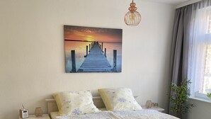 A bedroom with a bed, a nightstand, a bedside table, a lamp, a painting, and a window with curtains. - Vacation at the Baltic Sea - beautiful vacation apartment for 4 persons (Warnow)