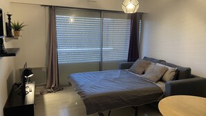 A modern bedroom with a bed, a sofa, a small table, and a ceiling light. - Grand Studio à la Coudouliere Proche de la Plage (Six-Fours-les-Plages)