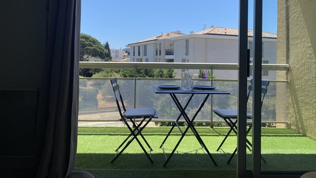 A balcony with a table and chairs, overlooking a green lawn and buildings in the background. - Grand Studio à la Coudouliere Proche de la Plage (Six-Fours-les-Plages)
