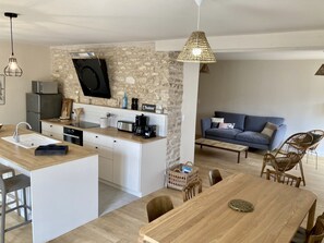 Una cocina moderna con pared de piedra, una isla integrada y una zona de comedor con mesa y sillas de madera.
