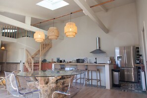 Una cocina moderna con una mesa de comedor de vidrio, lámparas colgantes de mimbre y un refrigerador de acero inoxidable.