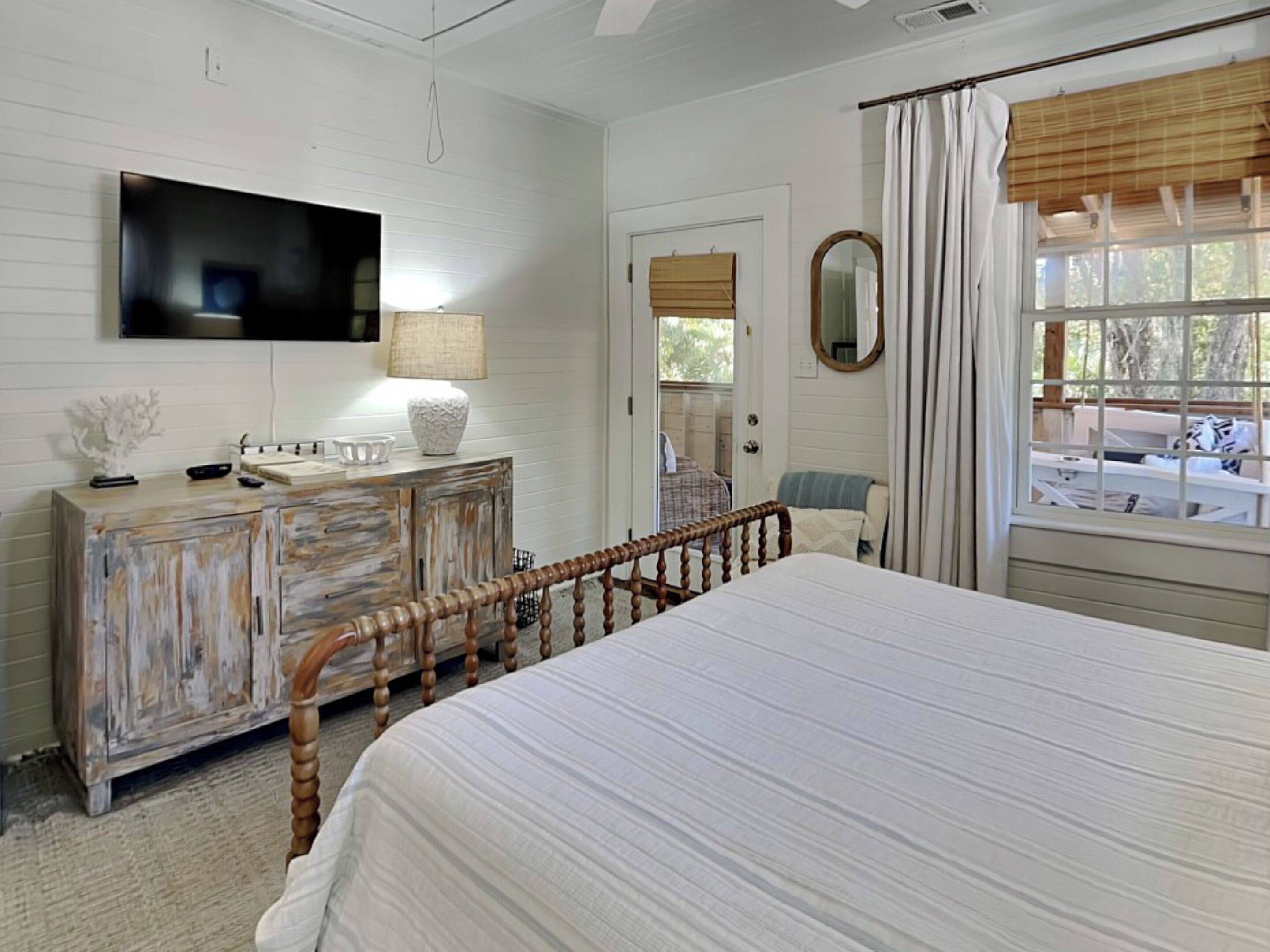 Un dormitorio con cama, cómoda, televisor, ventana con cortinas y puerta.