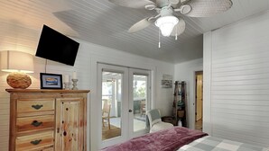 A bedroom with a bed, a wooden dresser, a ceiling fan, and a television on the wall. - The Fort | Private Pool, Fire Pit Arcade Games (Tybee Island)