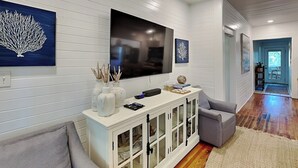 A modern living room with a flat-screen TV mounted on the wall, a white console table with glass doors, and a grey sofa. - The Fort | Private Pool, Fire Pit Arcade Games (Tybee Island)