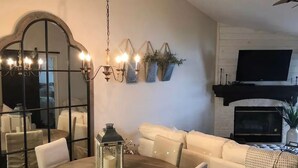Un'area pranzo con un tavolo rotondo, sedie bianche, un lampadario e una parete a specchio.
