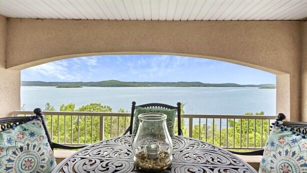 Un balcone con tavolo e sedie, affacciato su una vasta distesa d'acqua e una costa lontana.