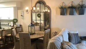 Zona pranzo con tavolo rotondo, sedie e lampadario. Si intravede una cucina sullo sfondo.