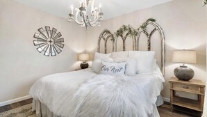 Una camera da letto con un letto grande, un lampadario, un elemento decorativo a parete e un comodino con una lampada.