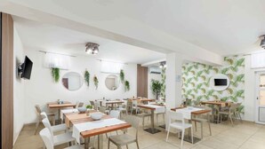 A modern dining area with multiple tables and chairs, a flat-screen TV mounted on the wall, and decorative plants. - Holiday apartment with terrace (Fažana)