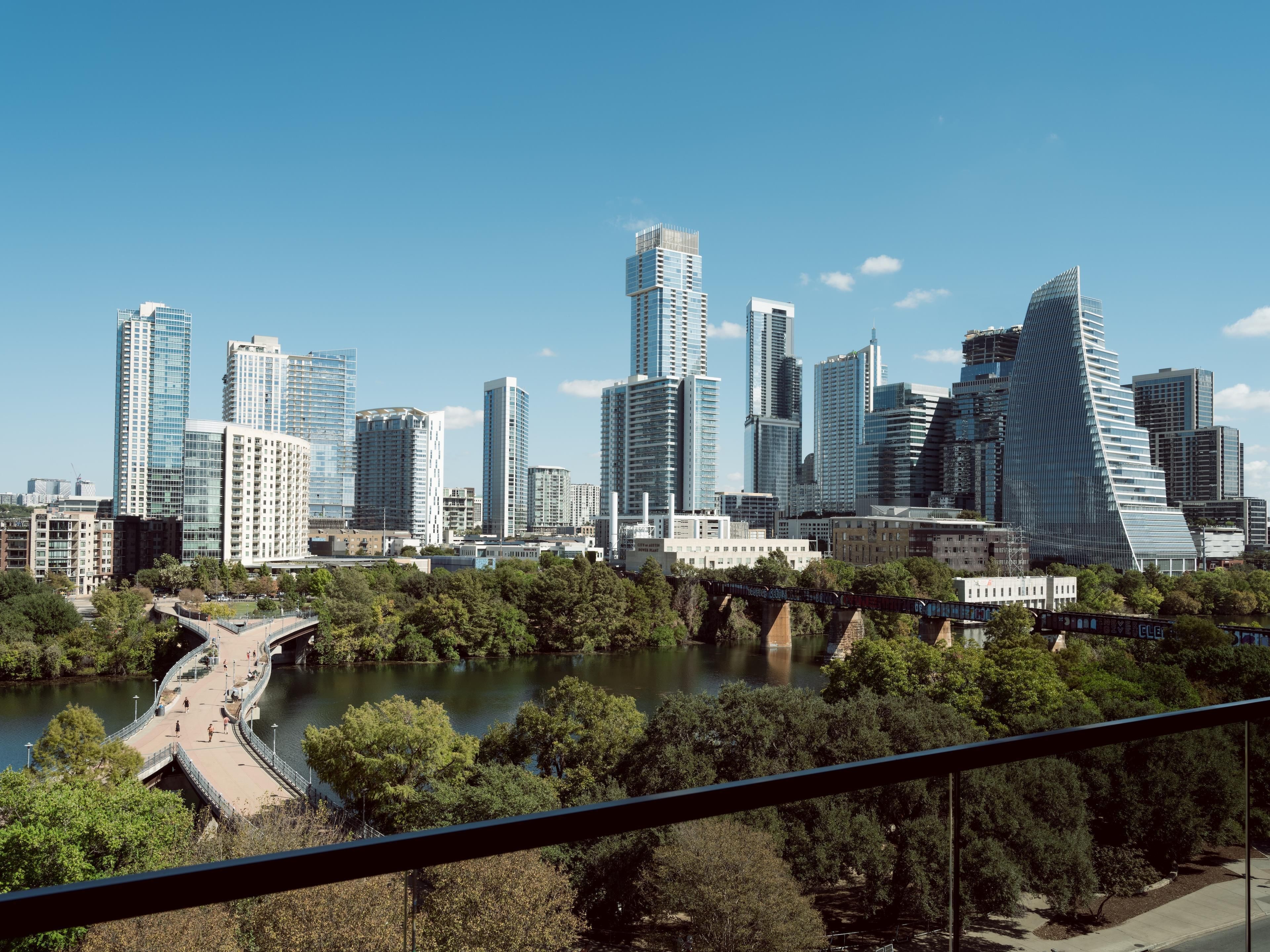A city skyline with modern skyscrapers and a river with a pedestrian bridge.