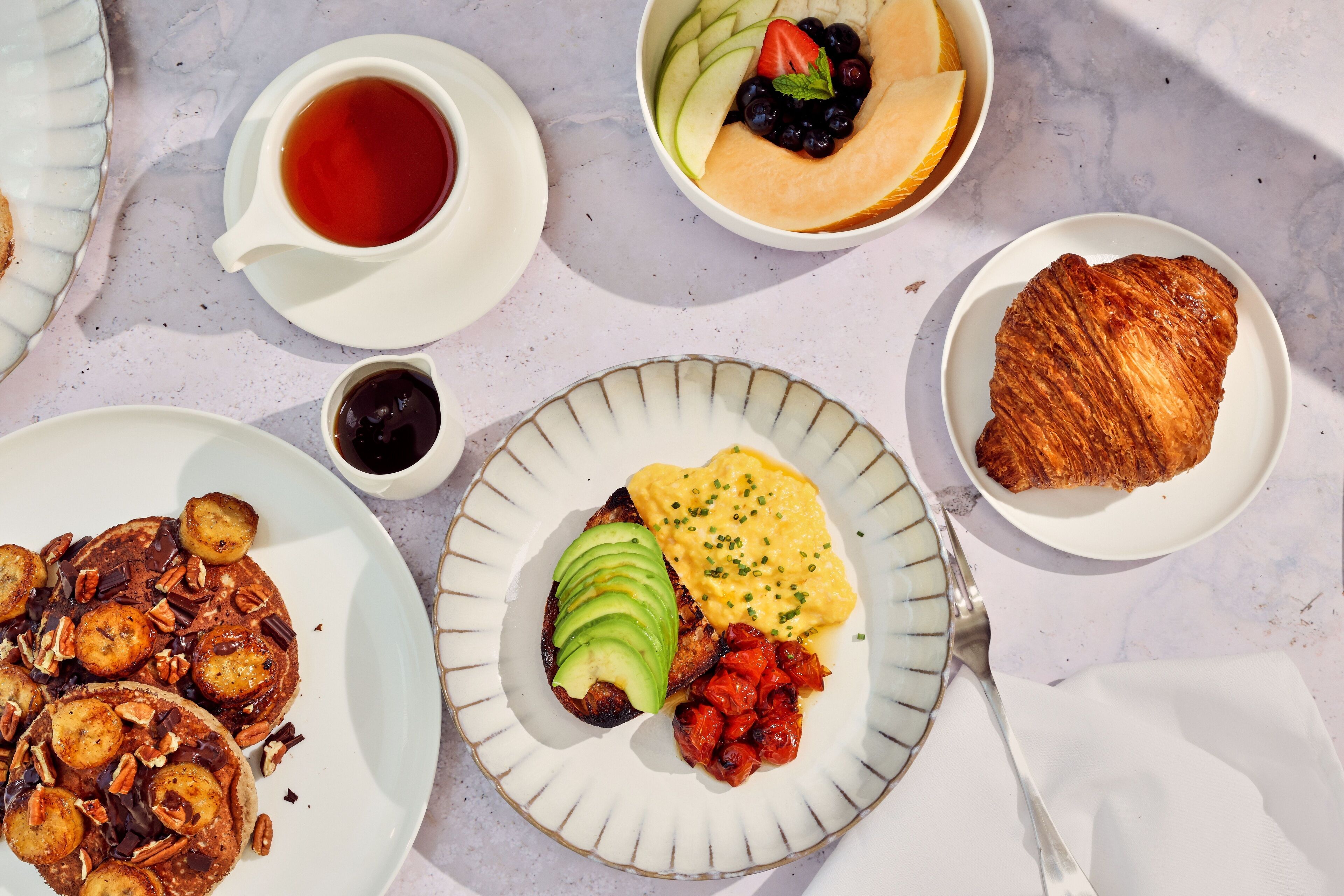 Un desayuno abundante con tortitas, huevos, tostadas y fruta en platos.