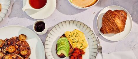 Un desayuno abundante con tortitas, huevos, tostadas y fruta en platos.
