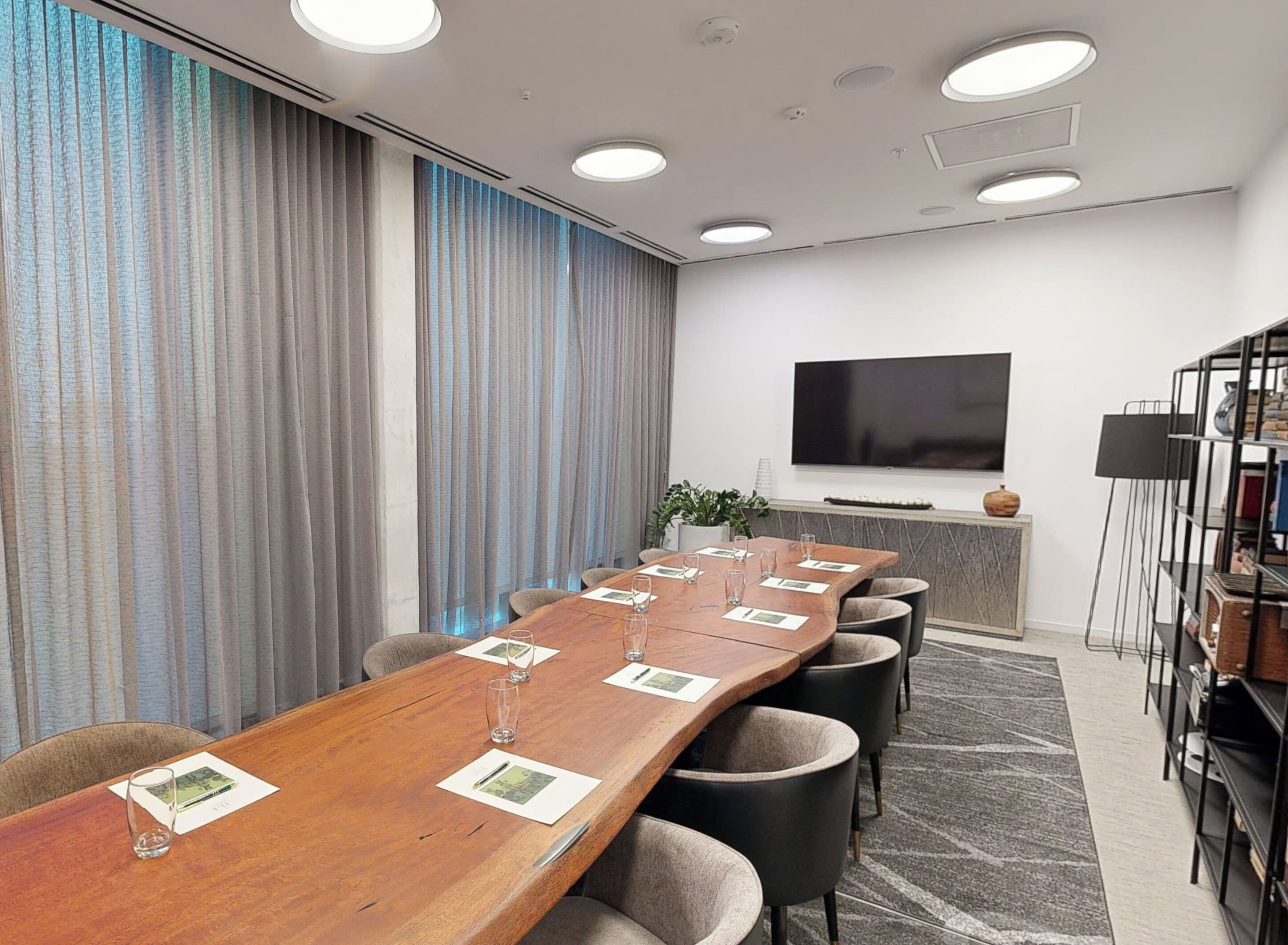 Une salle de conférence avec une longue table en bois, plusieurs chaises, un téléviseur à écran plat et une bibliothèque.
