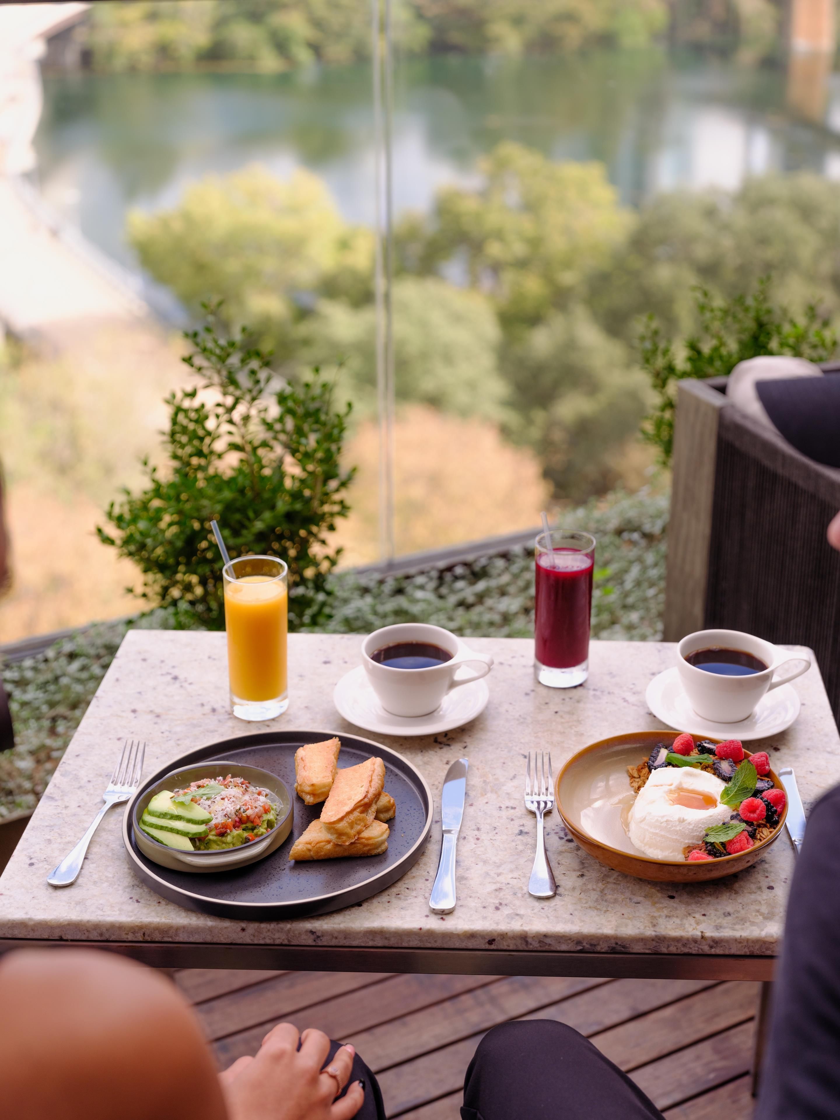 A table with breakfast items, including pancakes, fruit, and coffee, overlooking a scenic view.