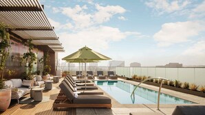 A rooftop pool area with lounge chairs and umbrellas, surrounded by potted plants and a city skyline view. - The Loren Hotel Austin, WorldHotels Luxury (Austin)