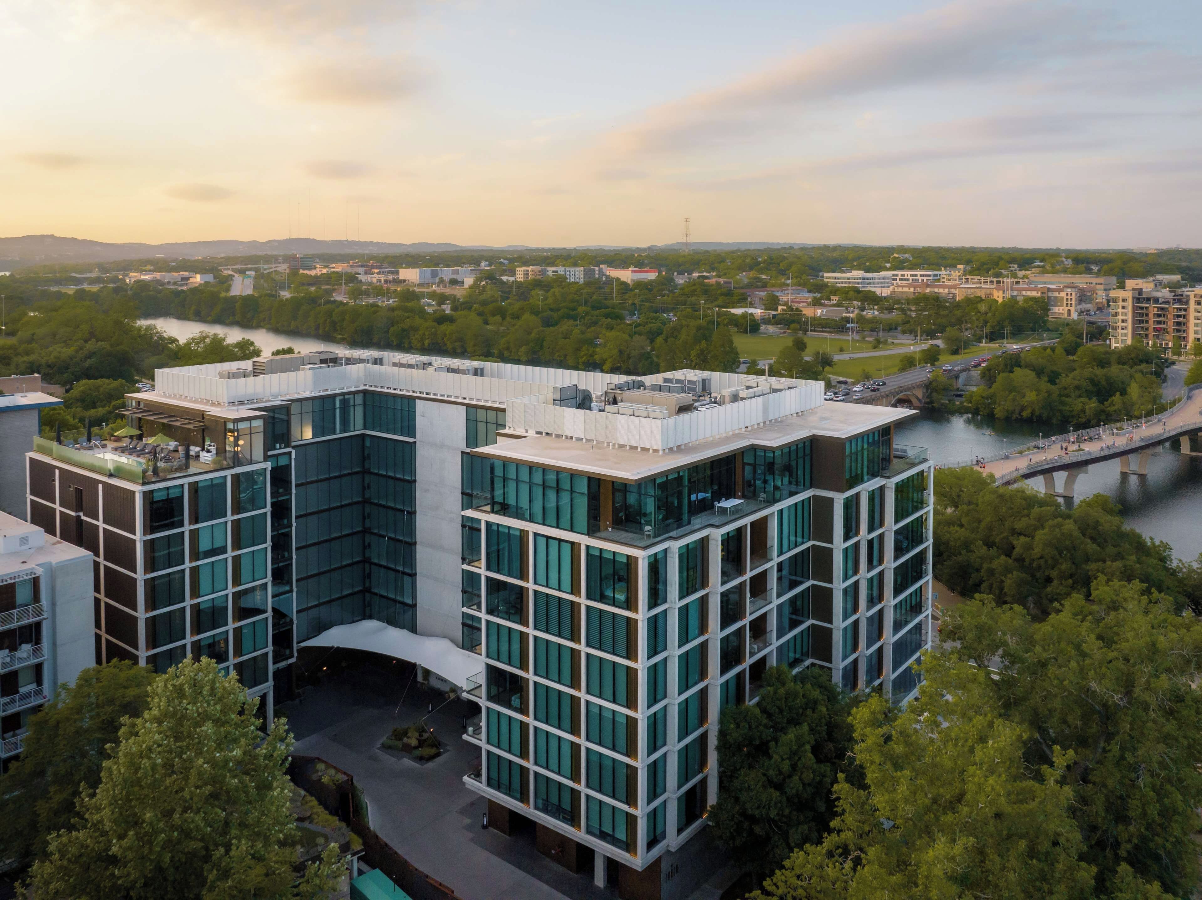 A modern building with a glass facade, surrounded by greenery and a river.
