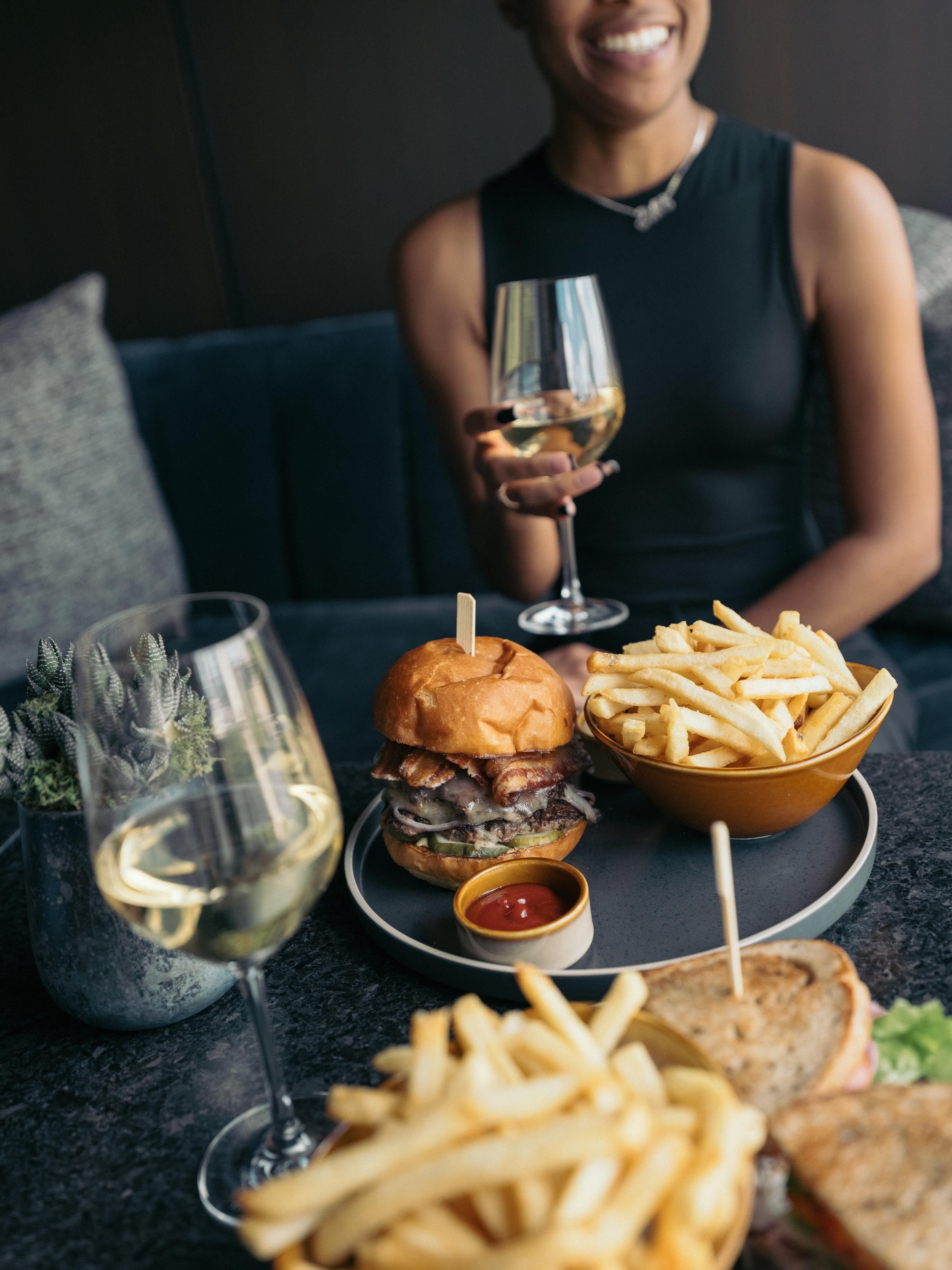 Een eettafel met een hamburger, friet en een glas witte wijn.