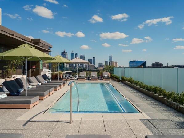 A rooftop pool area with lounge chairs and umbrellas, a clear view of the city skyline in the background. - The Loren Hotel Austin (Austin)