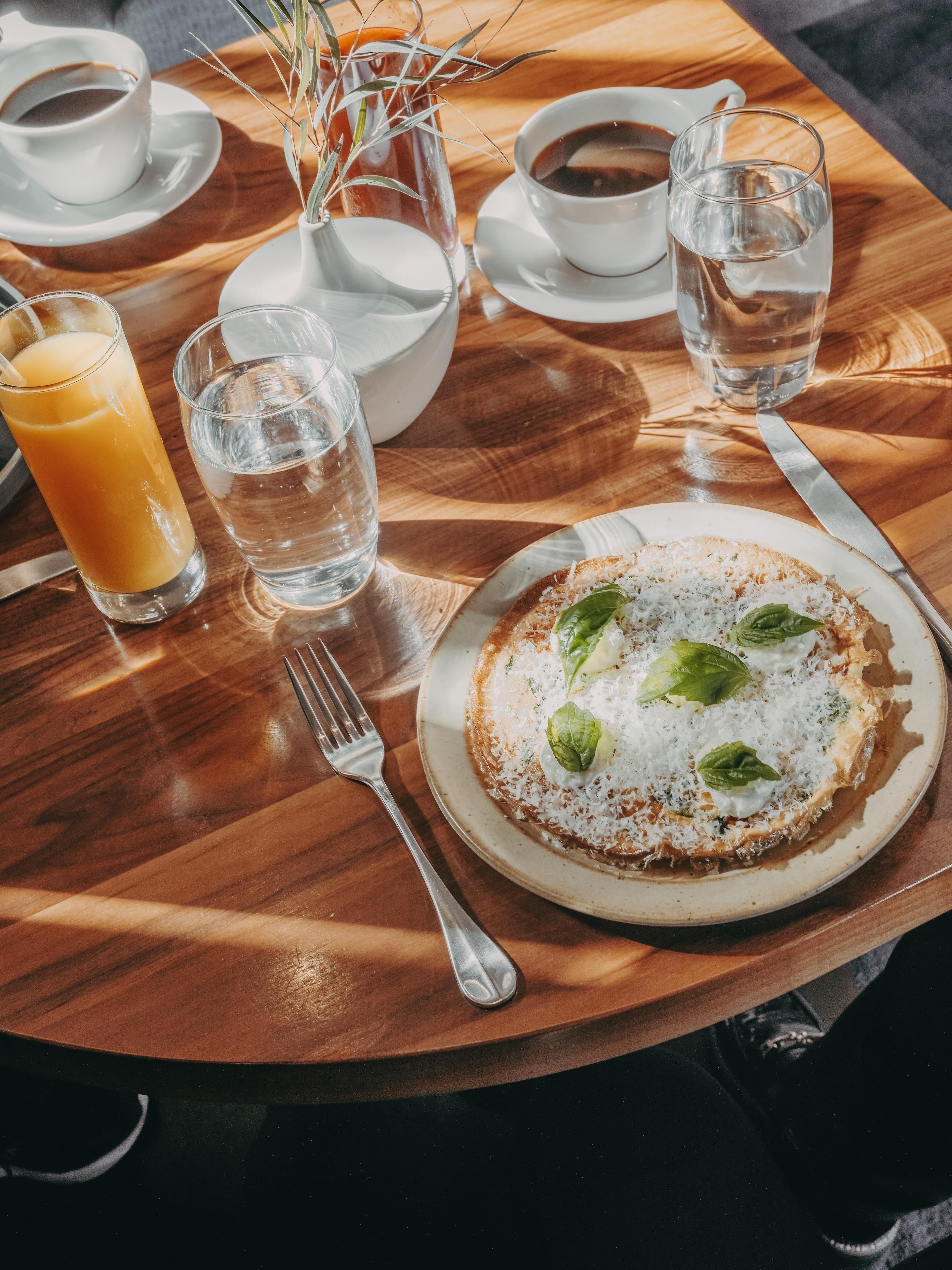 Ein Holztisch mit einem Teller Essen, einem Glas Orangensaft und einem Glas Wasser.