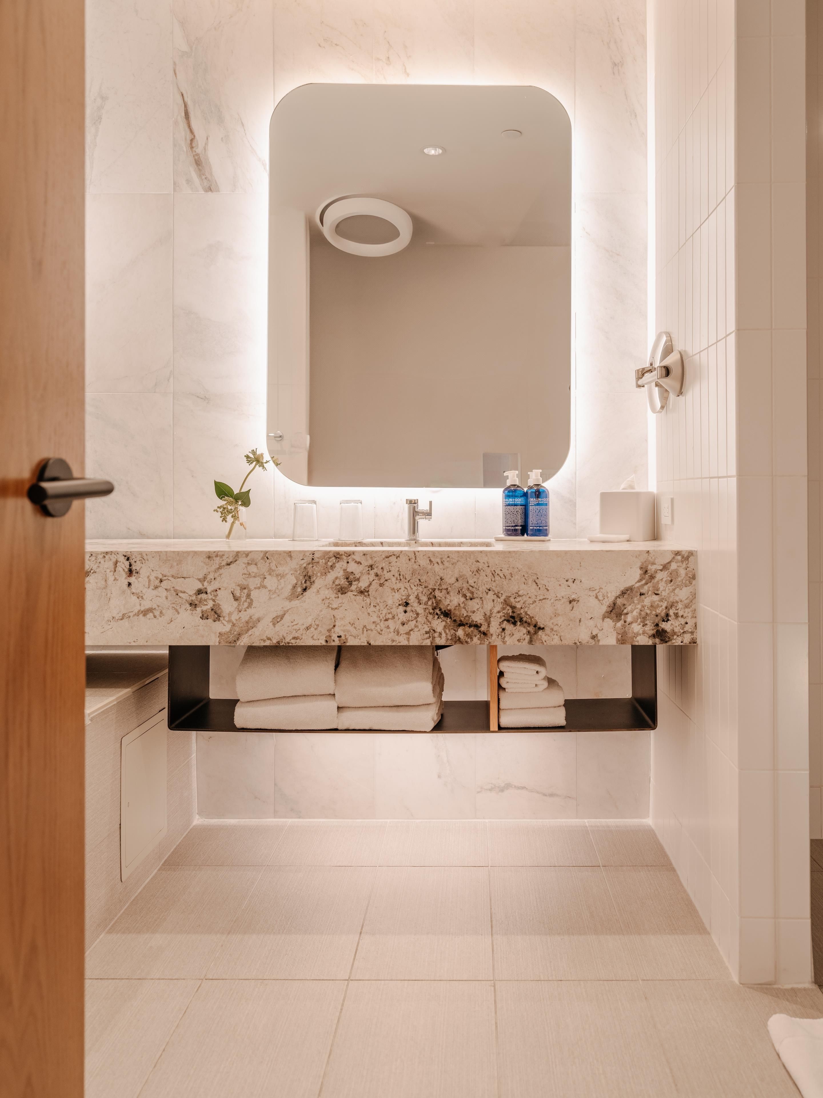 Un baño moderno con tocador de mármol, un espejo grande y toallas dobladas con cuidado.
