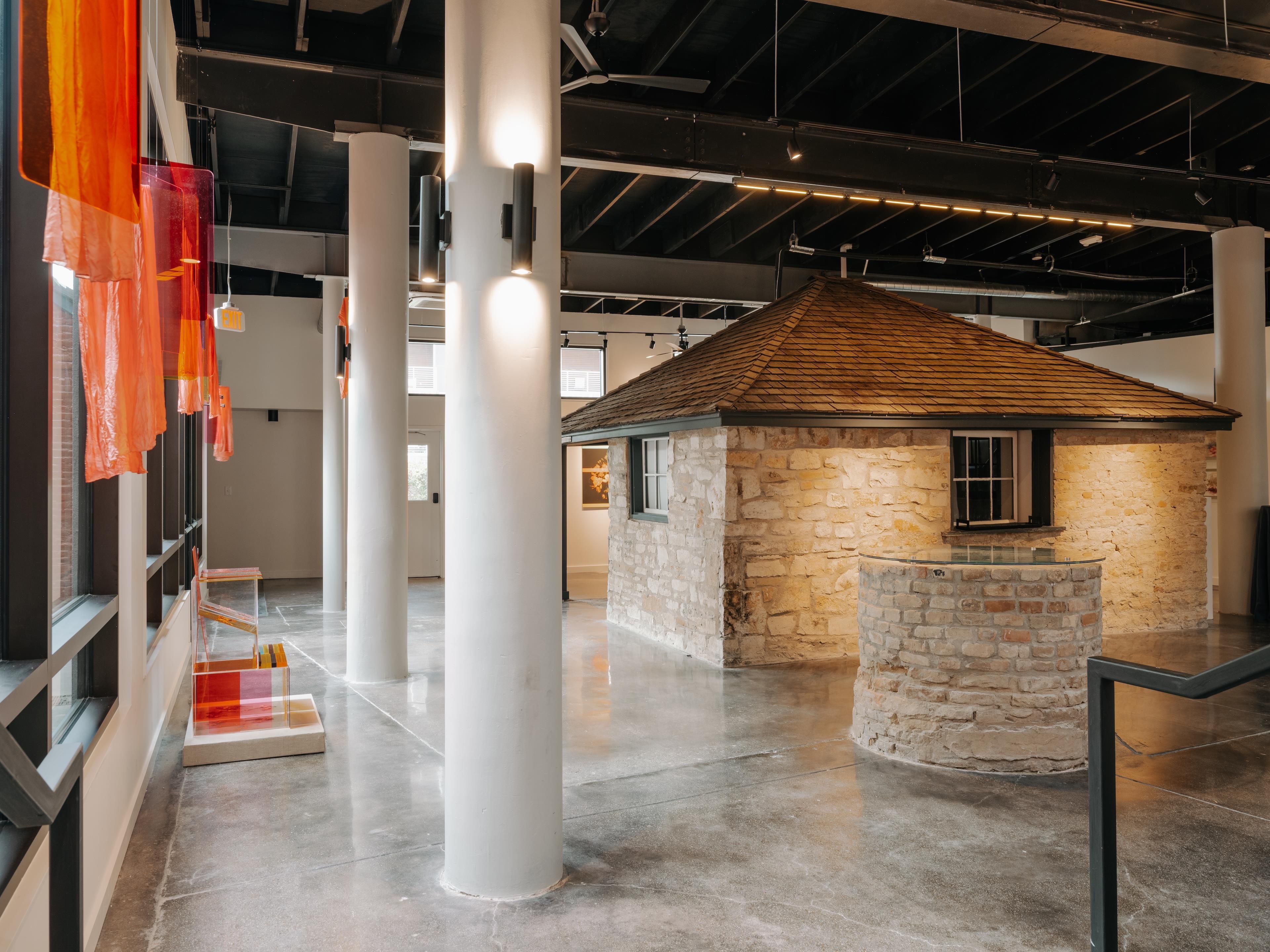 A spacious indoor area with high ceilings, large white columns, and a small stone building with a tiled roof.