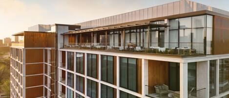 A modern building with a glass facade, multiple balconies, and a rooftop terrace.