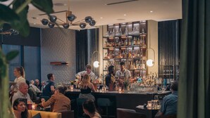 A bar area with patrons seated at tables, a bartender preparing drinks, and shelves stocked with bottles and glasses. - The Loren Hotel Austin, WorldHotels Luxury (Austin)