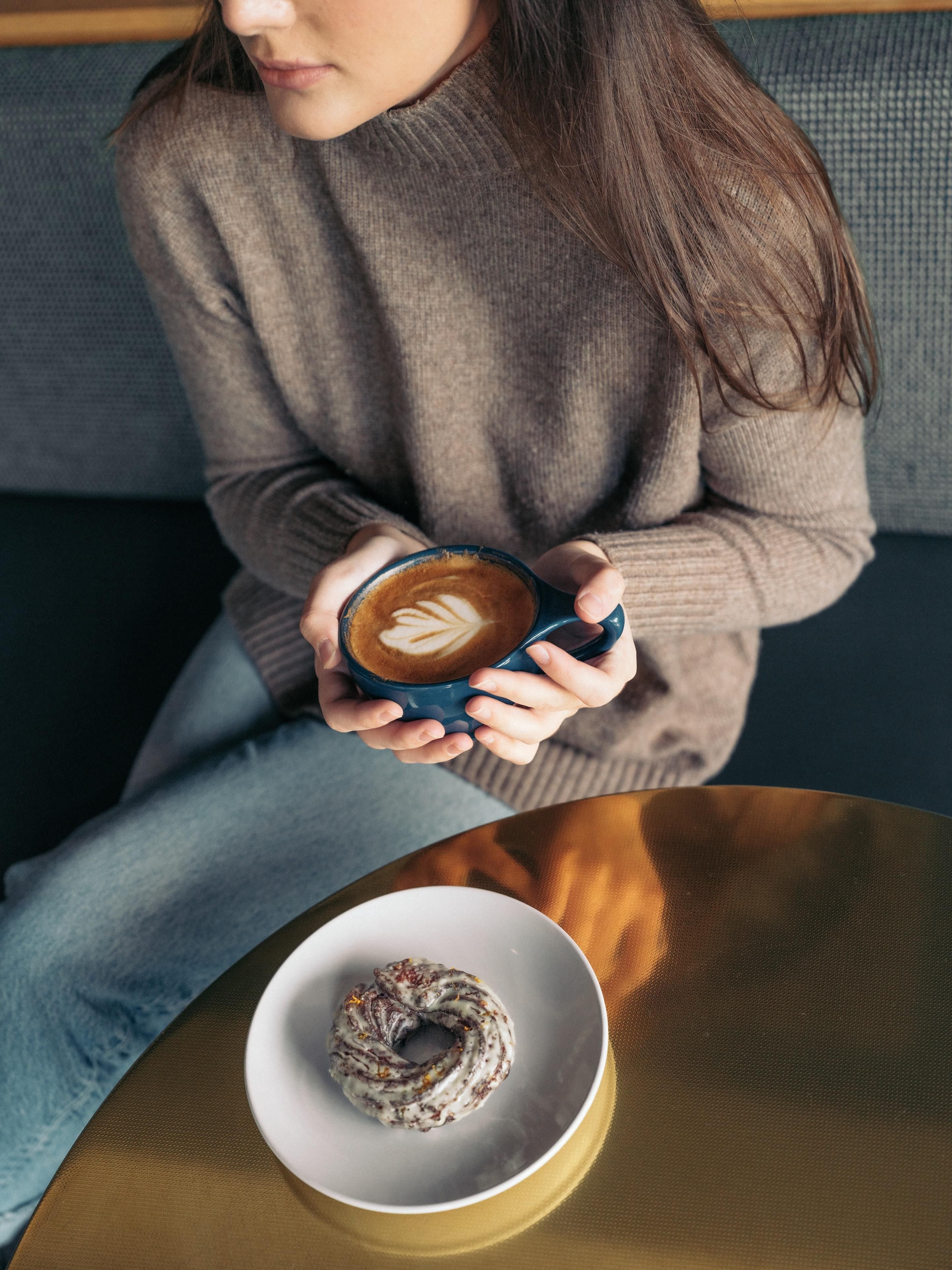 Una persona sosteniendo una taza de café con arte de latte, sentada en un sofá.