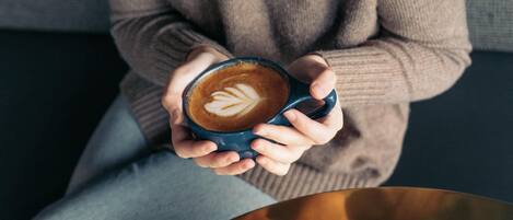 Una persona sosteniendo una taza de café con arte de latte, sentada en un sofá.