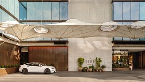 Un edificio moderno con fachada de vidrio, un automóvil blanco estacionado al frente y una amplia estructura tipo marquesina.