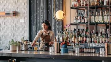 Zona de bar con un barman preparando bebidas, estanterías llenas de diferentes botellas de licor y un diseño de interiores moderno.