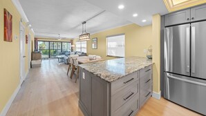 A modern kitchen with a large island, stainless steel appliances, and a dining area with a view. - Beachfront Paradise + Complimentary Sanibel Recreation Center Family Pass! (Sanibel Island)