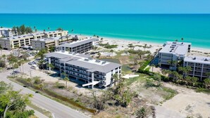 A coastal hotel complex with multiple buildings, a parking area, and a view of the ocean. - Beachfront Paradise + Complimentary Sanibel Recreation Center Family Pass! (Sanibel Island)
