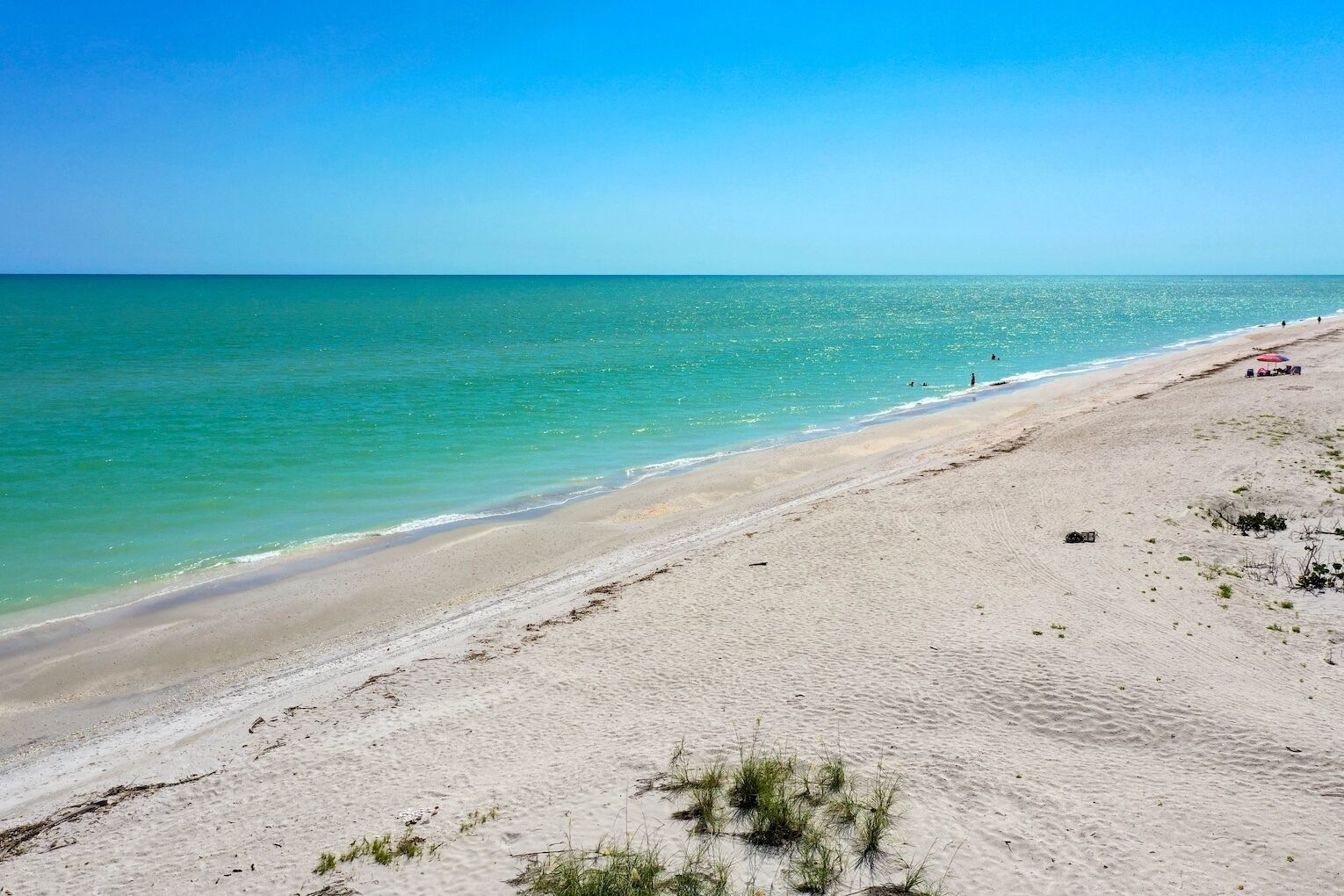 A beach with clear turquoise water, sandy shore, and a few umbrellas.