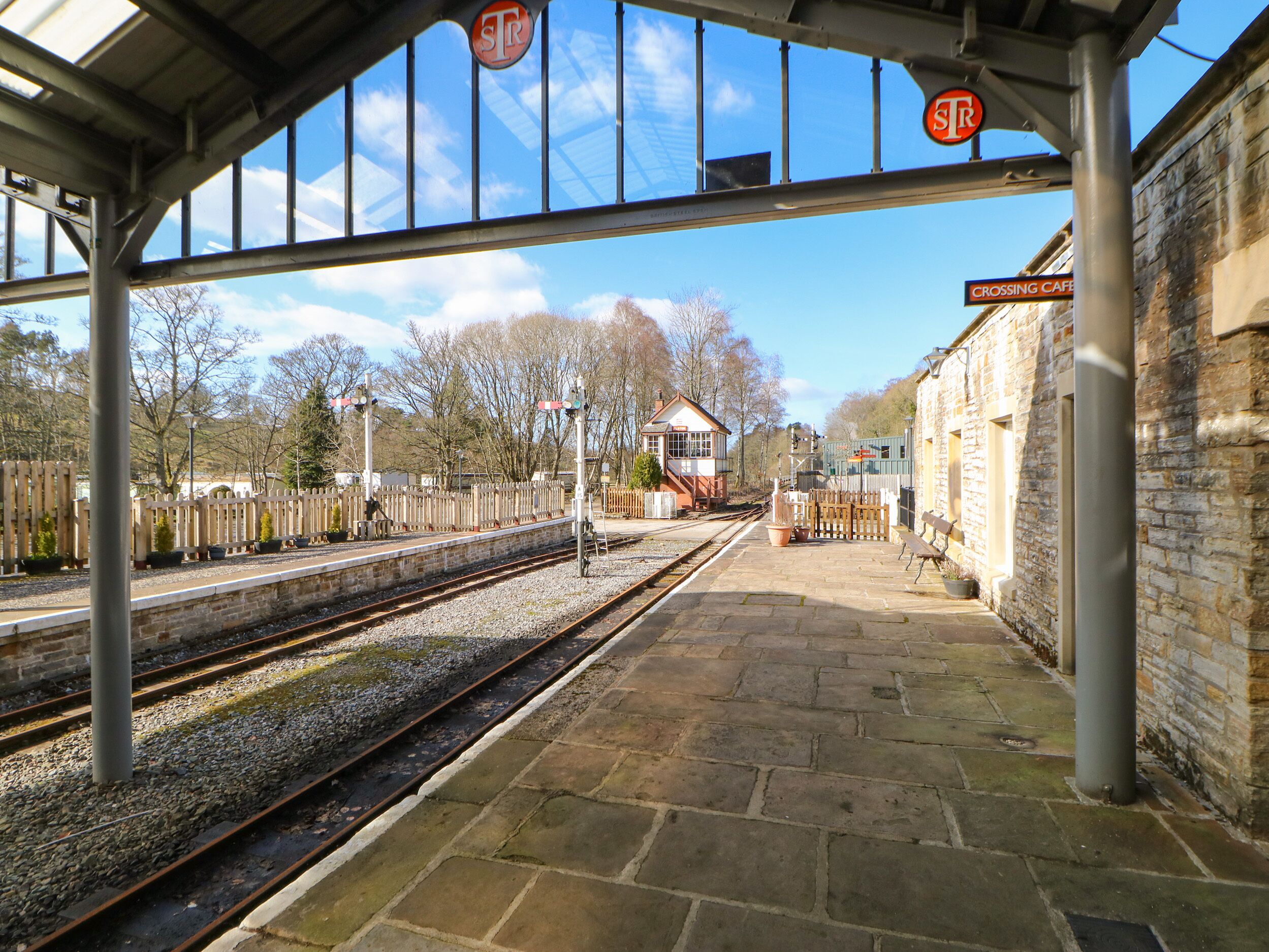 Un quai de gare avec un sol en pierre, un espace d’attente abrité et une clôture en bois.