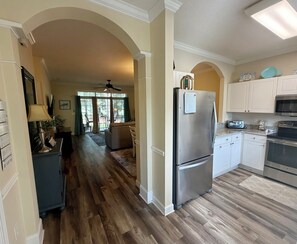 A kitchen with a stainless steel refrigerator, white cabinets, and a wooden floor.