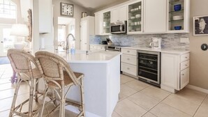 Une cuisine moderne avec des meubles blancs, un îlot central et un coin repas doté de chaises en osier.