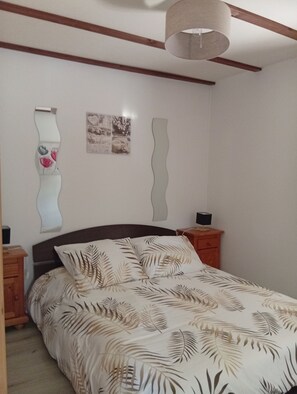 Een slaapkamer met een bed, houten hoofdbord, nachtkastjes, een spiegel aan de muur en een plafondlamp.