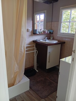 Een kleine badkamer met een douche, wastafel, spiegel en raam.