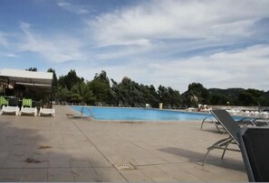 A swimming pool with lounge chairs and a covered area, surrounded by trees and a clear sky.