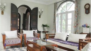 Une pièce avec un sol à carreaux, des meubles en bois, une table basse avec un plateau en verre et une grande fenêtre avec des rideaux.