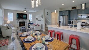 A modern kitchen with a central island, a dining area with a wooden table set for four, and a cozy living room with a fireplace.