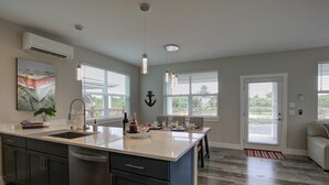 A modern kitchen with a central island, a dining area with a view, and a living space with a sofa and a door.