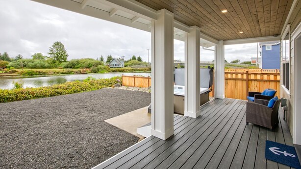 A covered outdoor deck with a view of a lake, wooden deck flooring, and a seating area with a chair and a table.