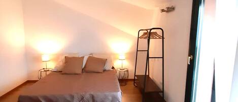 A bedroom with a bed, bedside lamps, a hanging rack, and a large window.