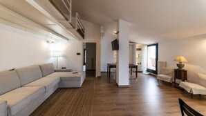 Een moderne woonkamer met een modulaire bank, een eethoek en een trap naar een hoger gelegen verdieping.