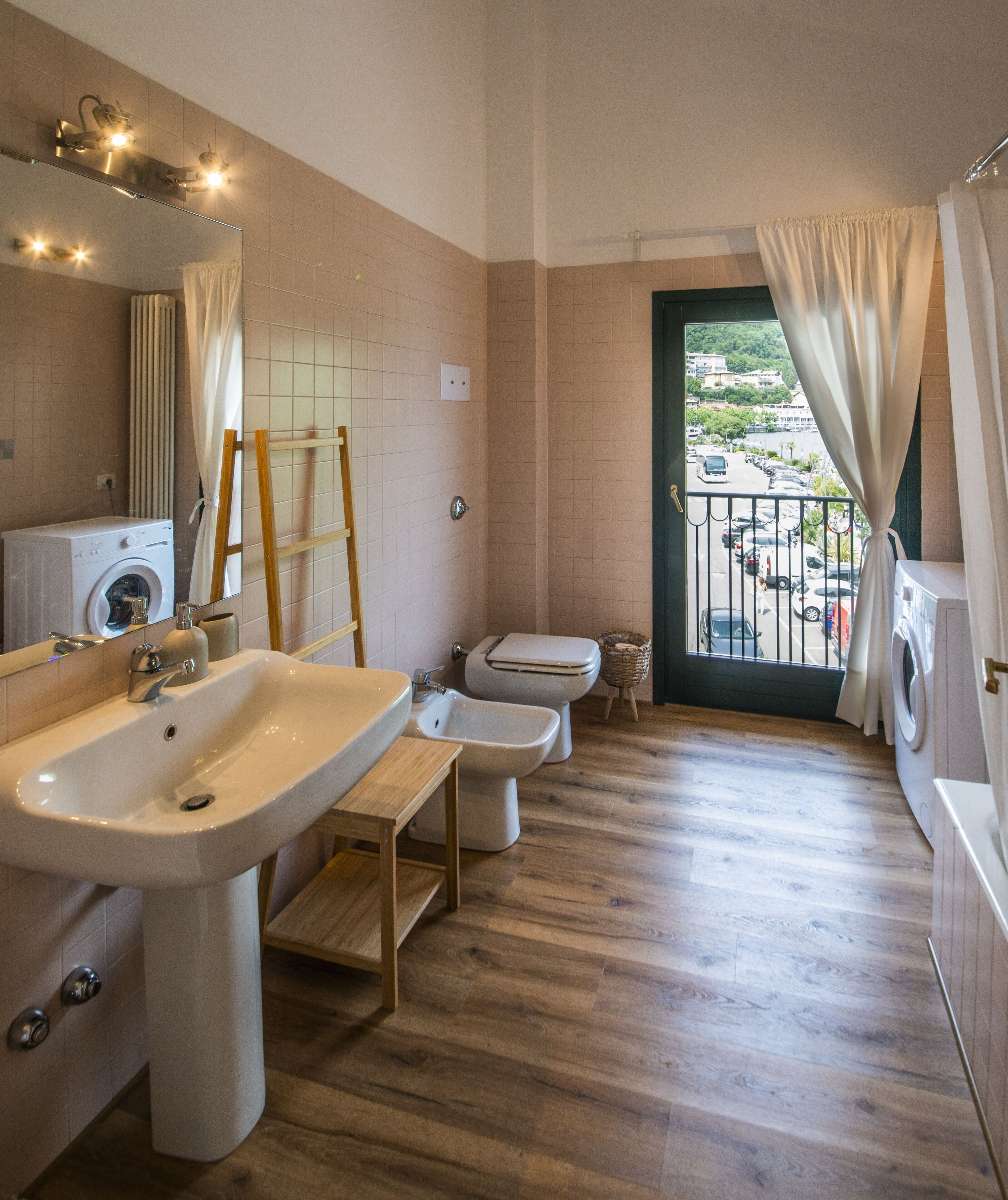 A modern bathroom with a large sink, a toilet, and a bidet. There is a mirror above the sink and a window with curtains.